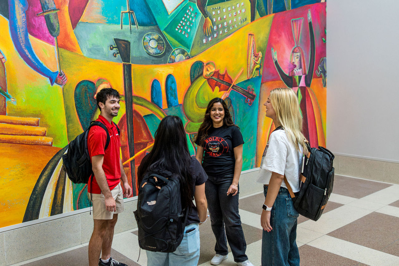 Four students talk in front of the Mary Emery Hall mural in the CCM Village.