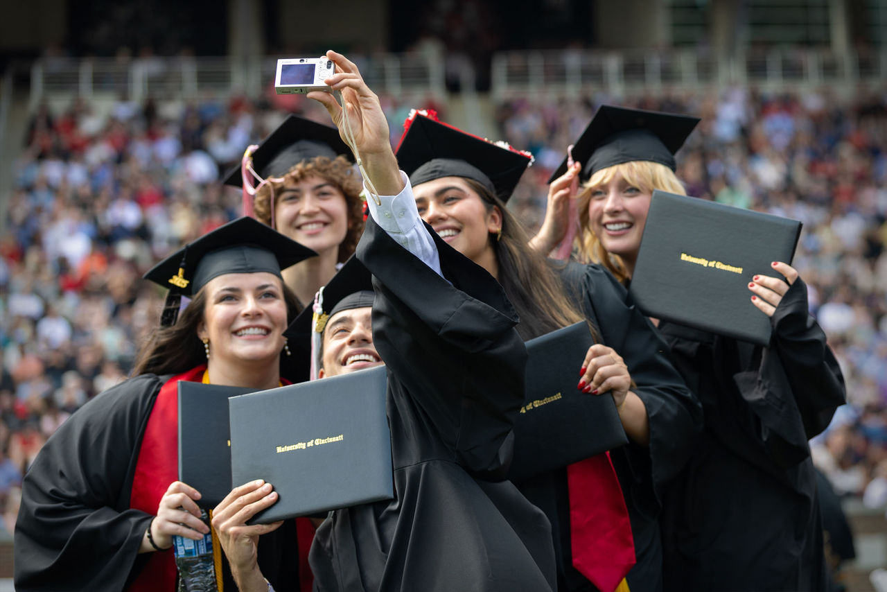 Five CCM students in caps and gowns pose for a selfie during graduation ceremony