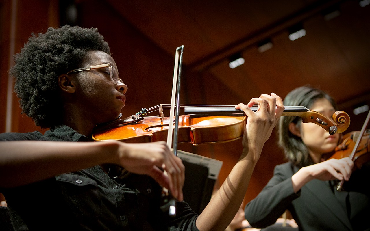 Close-up of a two female violin students performing on the Corbett Auditorium stage with the CCM Concert Orchestra