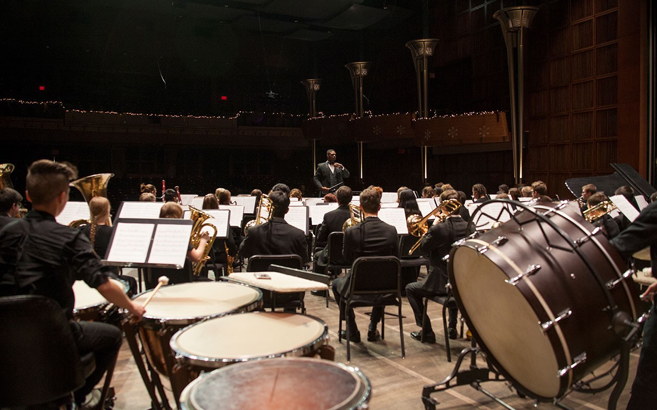 A wind ensemble rehearses on stage